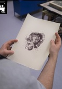 Na zdjęciu widać dłonie uczestnika pracowni, trzymające czarno-białą grafikę.