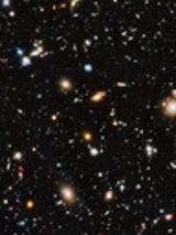 Zdjęcie przedstawia widok kosmosu z teleskopu Hubble'a. Różnobarwne gwiazdy świecą na ciemnym tle.