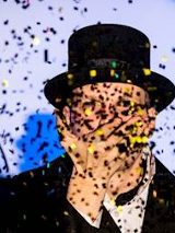 Fotografia mężczyzny w cylindrze a przed nim padające konfetti.