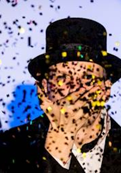 Fotografia mężczyzny w cylindrze a przed nim padające konfetti.