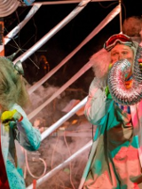 Na zdjęciu widać dwoje naukowców, kobietę i mężczyznę o siwych, bujnych włosach. Bohaterka Nielemka ubrana jest w czerwony kombinezon oraz biały fartuch opatrzony różnymi wzorami chemicznymi i matematycznymi. Bohater Lemtak ma widoczne na czole okulary i dmucha w rurę wentylacyjną, z której wylatuje dym.