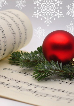 Zdjęcie zeszytu z nutami a na nim gałązka świerku i czerwona bąbka.