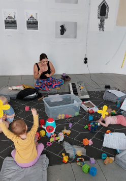 Mamy z dziećmi siedzące na podłodze. Wokół rozrzucone zabawki.