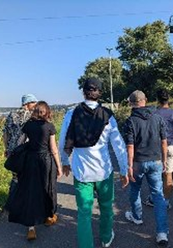 Grupa osób spaceruje, wokół zieleń.