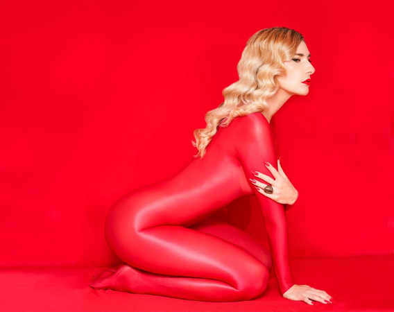 Blondynka w czerwonym, lateksowym stroju na tle czerwonej ściany.