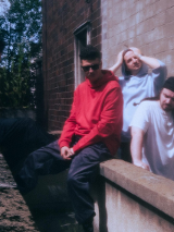 Czterech mężczyzn siedzi i stoi przy murku obok ściany budynku.