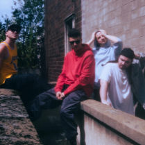 Czterech mężczyzn siedzi i stoi przy murku obok ściany budynku.