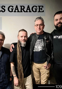 Kilku mężczyzn stoi w pomieszczeniu, w tle ściana, nad nimi napis informujący o nazwie zespołu i dacie koncertu.