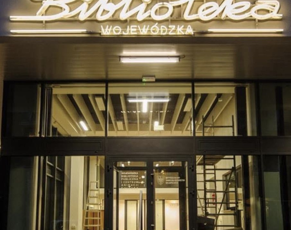 Budynek Biblioteki Wojewódzkiej nocą. Nad wejściem jasny neon.