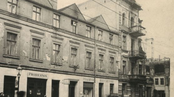 Czarno-białe zdjęcie budynku przy ulicy, po której chodzą przechodnie.