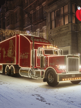 Rozświetlona, czerwona ciężarówka z logiem Coca Cola. Na boku rysunek świętego Mikołaja.