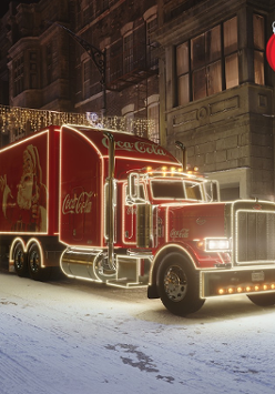 Rozświetlona, czerwona ciężarówka z logiem Coca Cola. Na boku rysunek świętego Mikołaja.