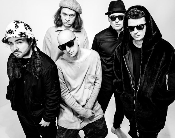 Członkowie zespołu spoglądają lekko w górę. Zdjęcie jest czarno-białe.