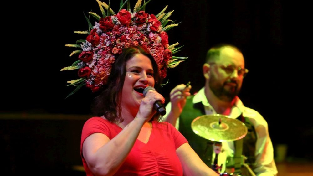 Dagmara Gregorowicz śpiewa do mikrofonu, na głowie ma duży, czerwono-zielony wieniec z kwiatów.