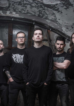 Zdjęcie pięciu mężczyzn w czarnych koszulkach, którzy stoją na tle odrapanej ściany.