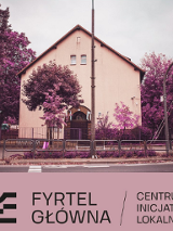 Budynek ze skośnym dachem i stojące przy nim fioletowe drzewa.