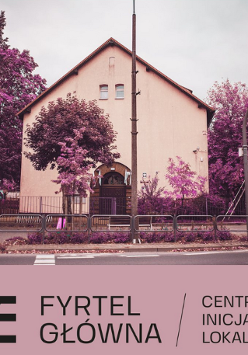 Budynek ze skośnym dachem i stojące przy nim fioletowe drzewa.