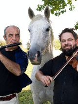 Dwóch mężczyzn grających na instrumentach i stojący pomiędzy nimi biały koń.