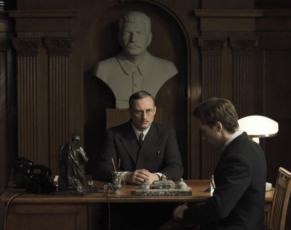 Dwaj mężczyźni przy biurku, za nim popiersie Stalina.