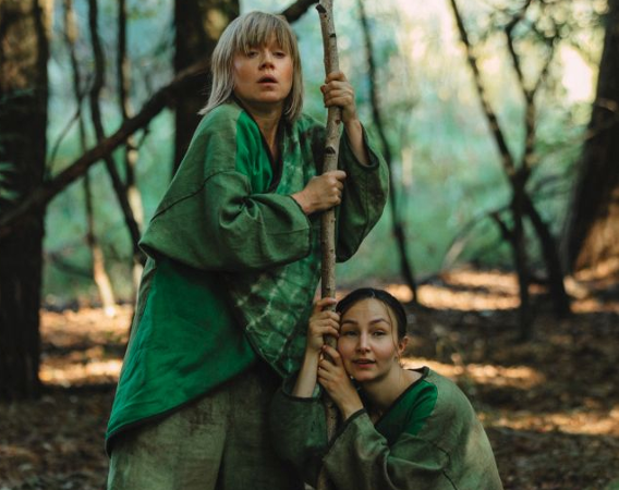 Dwie kobiety w zielonych strojach w lesie.