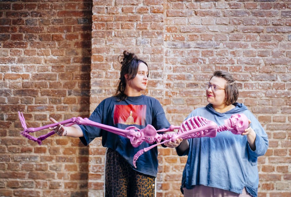 Dwie młode kobiety trzymają w rękach sztuczny fioletowy ludzki szkielet.