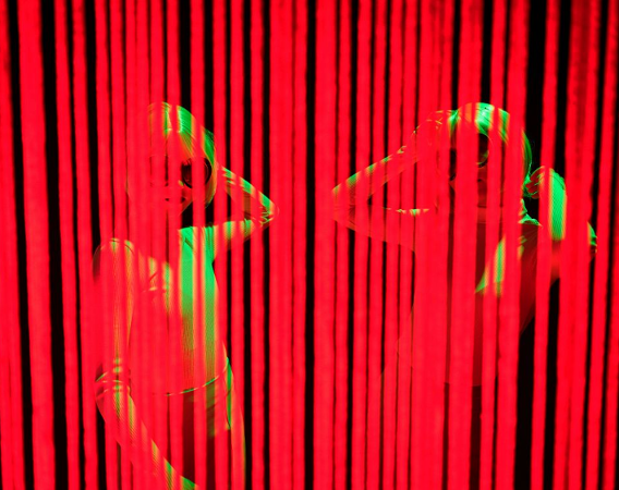 Dwie postaci kobiece za zasłoną z czerwonych pasków.