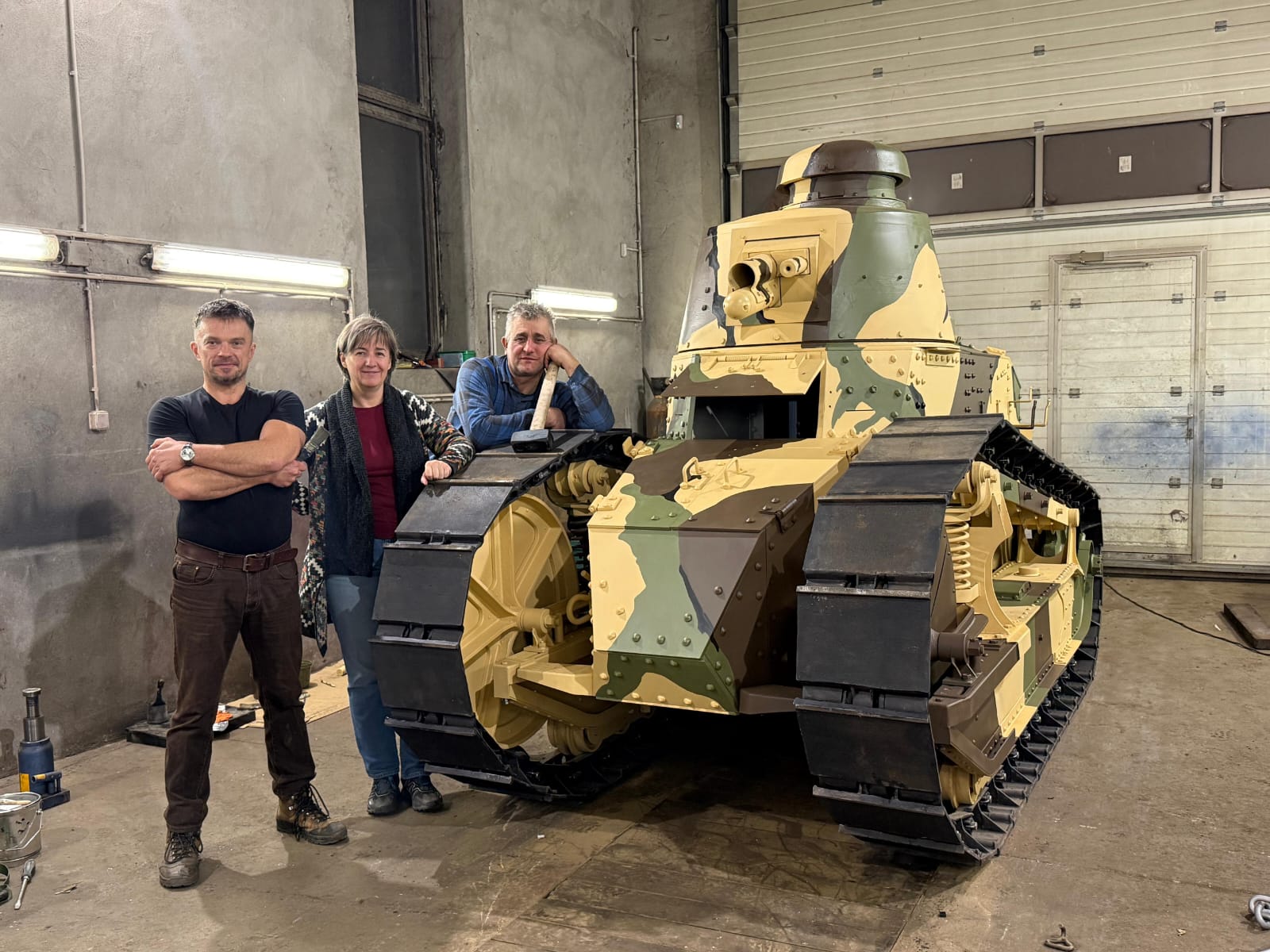 Dwóch mężczyzn i kobieta przy czołgu starego typu, malowanie pancerza w plamy, szerokie gąsienice