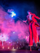 Aktorka na szczudłach w ręku trzymająca sztuczne ognie.