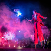 Aktorka na szczudłach w ręku trzymająca sztuczne ognie.