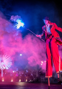 Aktorka na szczudłach w ręku trzymająca sztuczne ognie.