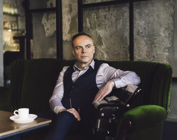 Elegancki mężczyzna z akordeonem siedzi w kawiarni.