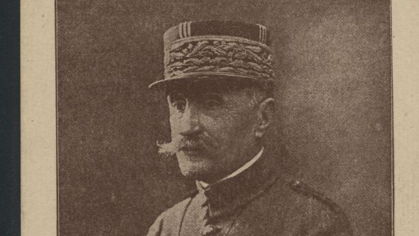 Czarno-białe zdjęcie mężczyzny w mundurze. Mężczyzna siedzi, na głowie ma czapkę z daszkiem, ręce opiera o uda.