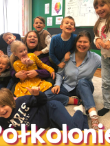 Roześmiane dzieci na dywanie. Wśród nich dwie roześmiane opiekunki "Półkolonie".