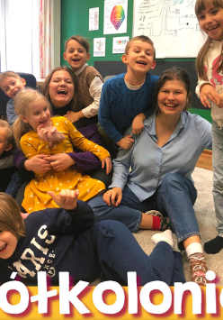 Roześmiane dzieci na dywanie. Wśród nich dwie roześmiane opiekunki "Półkolonie".