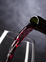 Kieliszek do którego nalewa się czerwone wino z zielonej butelki.