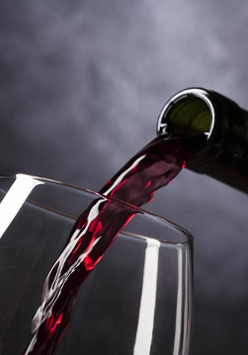 Kieliszek do którego nalewa się czerwone wino z zielonej butelki.