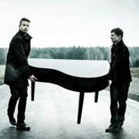 Na czarno-białym zdjęciu dwóch mężczyzn niosących fortepian.
