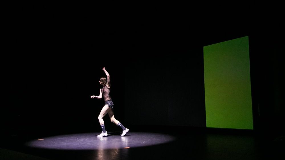 Podświetlony performer wykonuje taneczne ruchy na scenie.