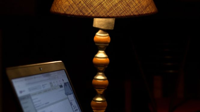 Otwarty laptop i lampka nocna na biurku. W tle ciemność.
