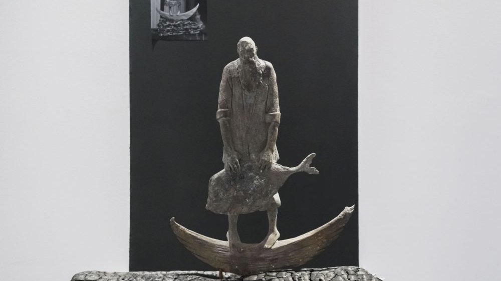 Rzeźba brodatego mężczyzny stojącego na łodzi i trzymającego w rękach złowioną rybę.