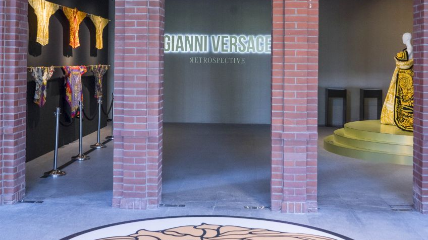 Wejście na wystawę. Na wprost podświetlony tytuł wystawy, na podłodze logo domu mody Versace.