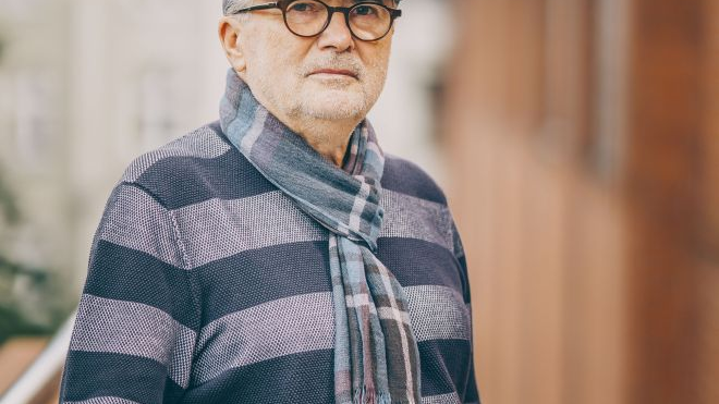 Piotr Soroka pozuje przy Starym Browarze, ma na sobie kaszkiet, pasiasty szalik i sweter.