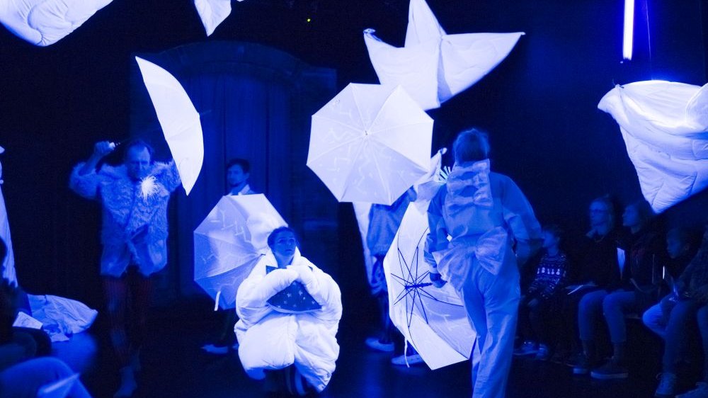 Scena ze spektaklu odgrywana w ciemności, z użyciem fluorescencyjnych parasoli.
