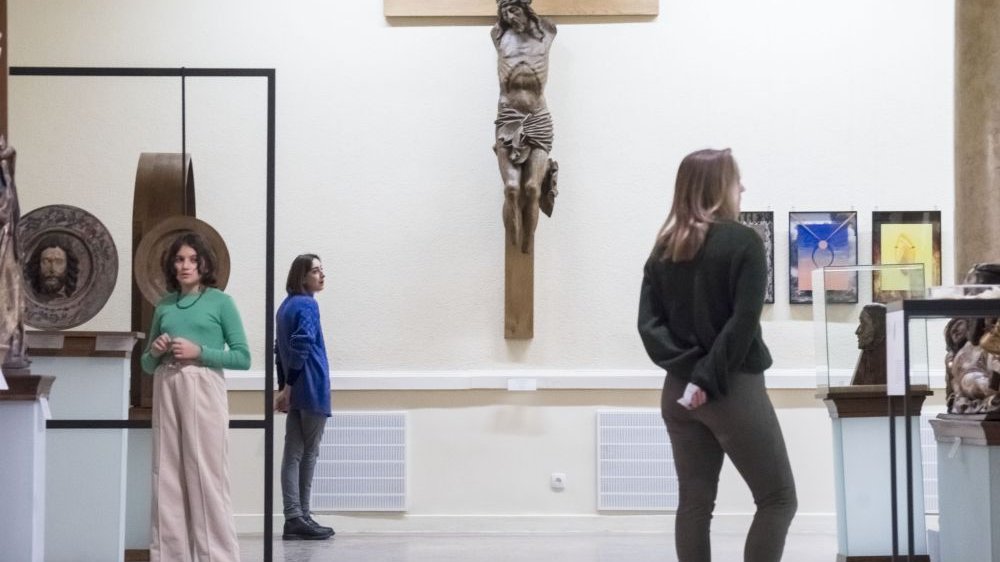 Rzeźba Jezusa na krzyżu nie ma rąk ani stóp. Krążą wokół niej widzowie wystawy.