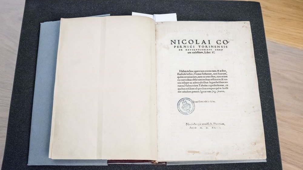 Strona tytułowa dzieła Mikołaja Kopernika. Pożółkły papier, pod tekstem widoczny exlibris Biblioteki Raczyńskich.