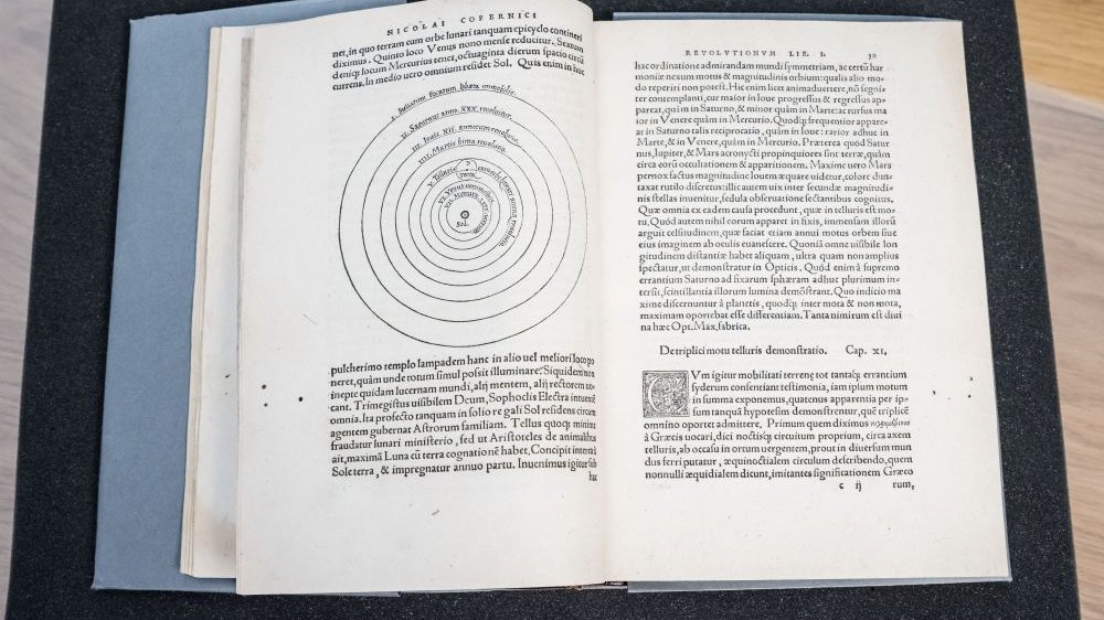 Zapisana po łacinie rozłożona księga. Na lewej stronie wykres układu planet.
