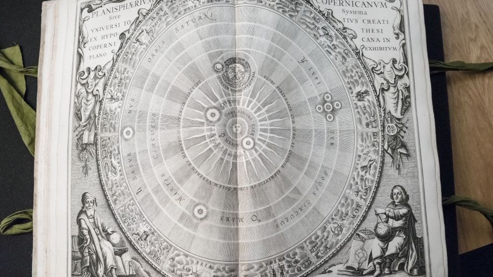 Rozłożona na rycinie księga "O obrotach sfer niebieskich" Mikołaja Kopernika.