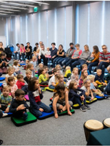 Spotkanie w sali. Dzieci siedzą na poduszkach na środku a dorośli na krzesłach dookoła.