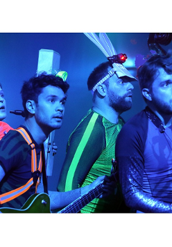 Na zdjęciu czworo młodych osób, stoją jeden za drugim, patrzą w tym samym kierunku, w rękach trzymają różne instrumenty muzyczne.