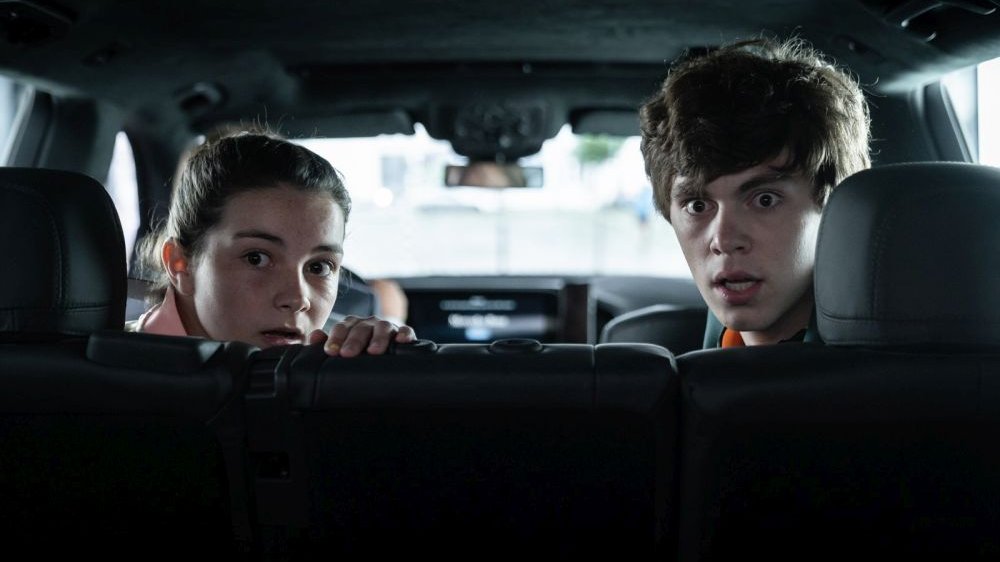 Młody chłopak oraz siedząca obok niego młodsza dziewczynka wyglądają przez tylną szybę samochodu, oboje mają przestraszony wzrok.